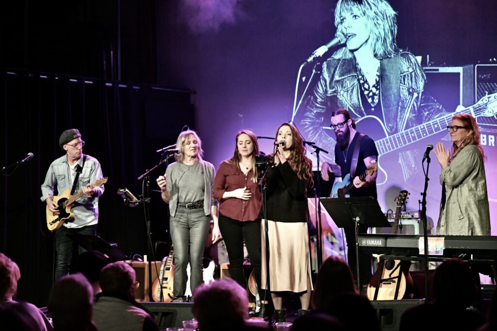 The Monday Night Live Band performs on th xBk Live stage. The lead singer stands in front while singing into a microphone.
